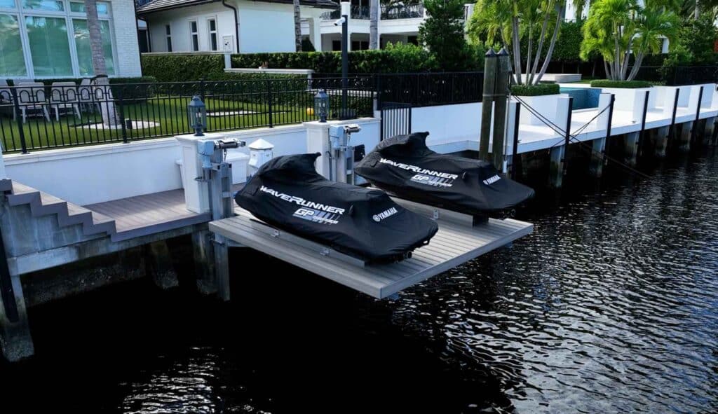 Two black jet skis on a dual jet ski platform lift at a seawall.