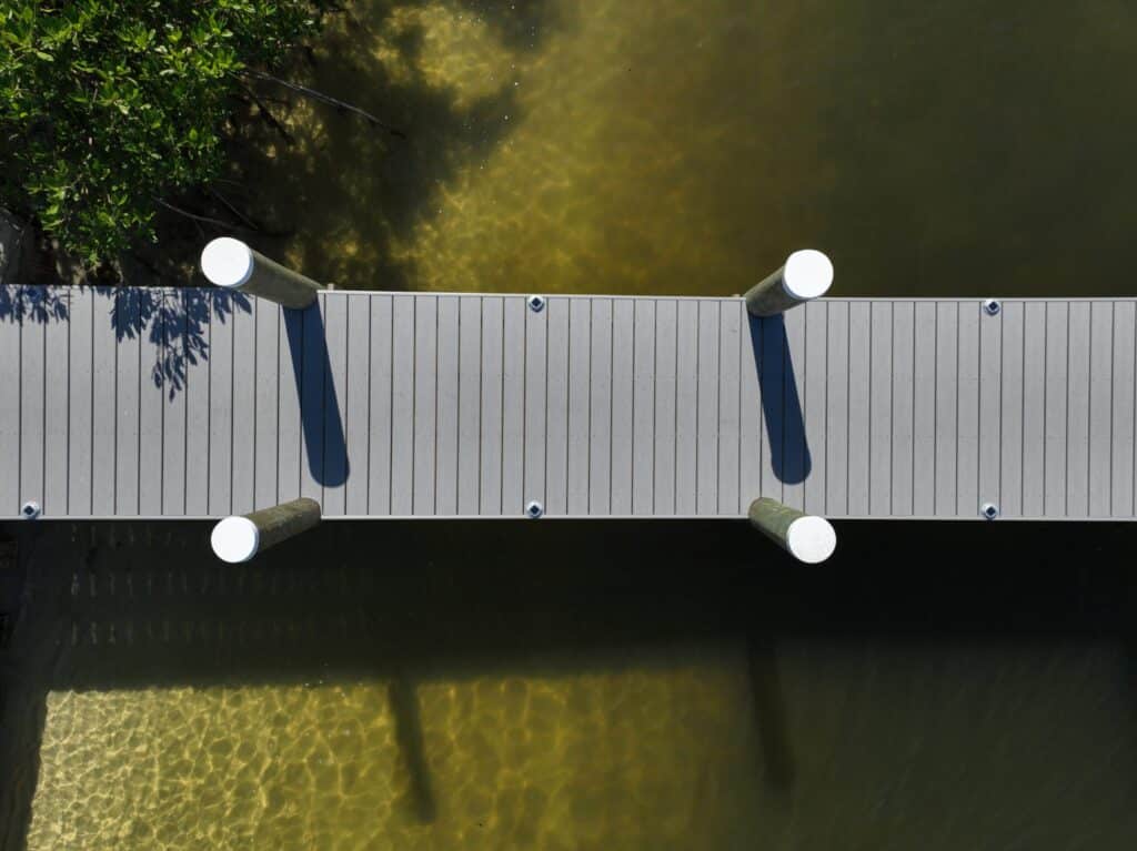 Top-down view of a gray composite dock walkway and pilings over shallow water in Tequesta.
