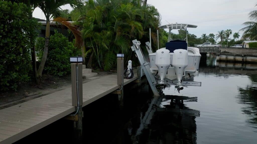 Boat with three outboard engines raised on an elevator boat lift beside a canal dock.